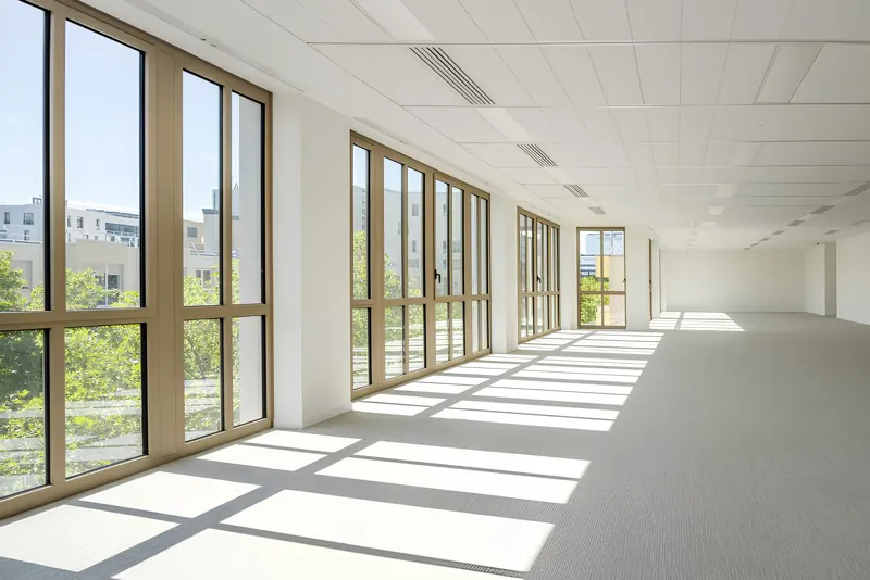 Plateau vide éclairé par une longue façade de menuiseries aluminium couleur bronze