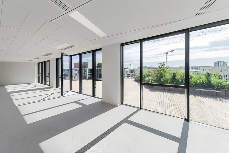 Plateau de bureaux baigné de lumière, grandes baies vitrées aluminium ouvrant sur une terrasse